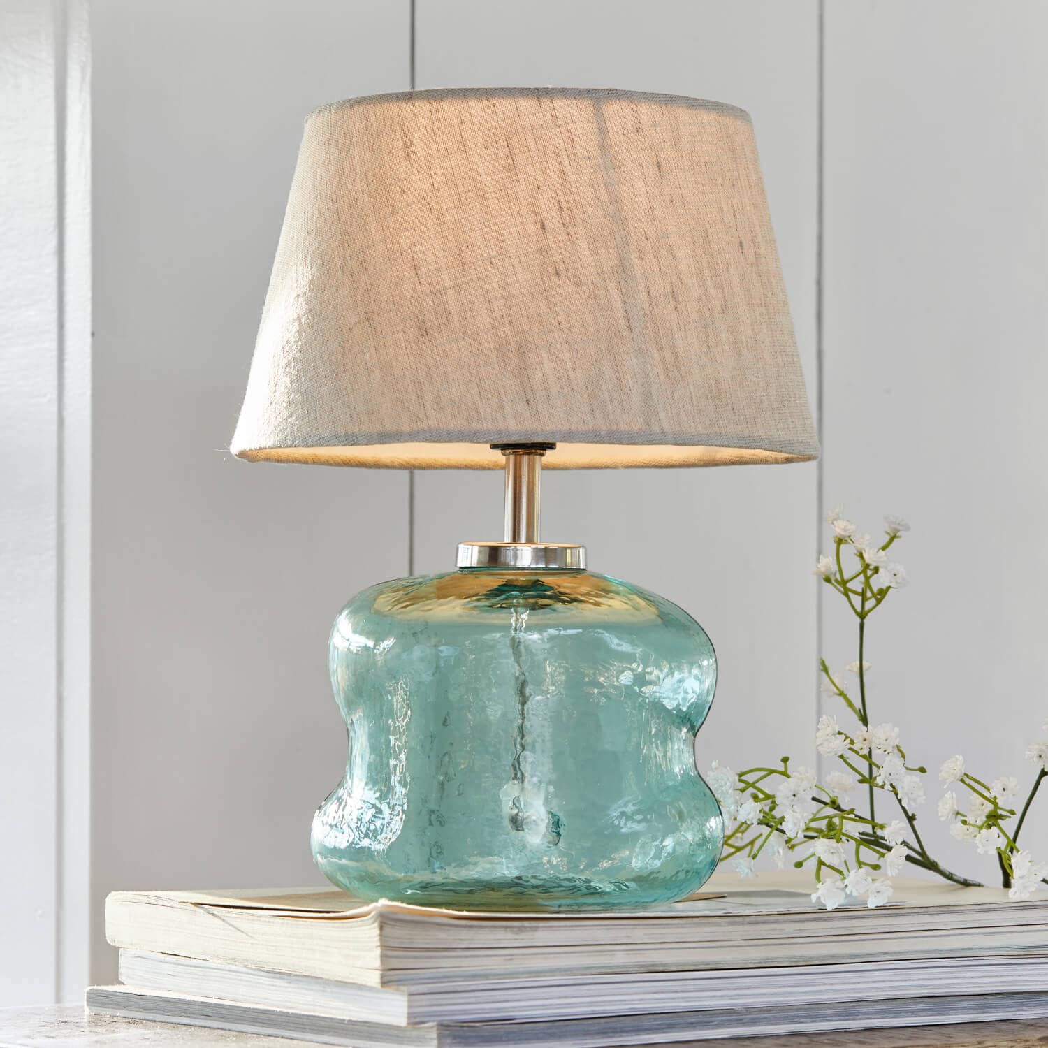 Tischlampe aus blauem Glas mit beigem Lampenschirm auf einem Bücherstapel, Wohnaccessoire