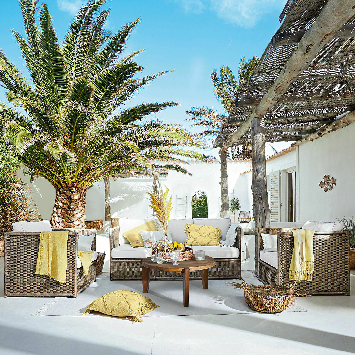 Sitzgruppe Lesmont Braunes Rattan-Gartenmöbel-Set mit cremefarbenen Polstern und gelben Akzenten auf sonniger Terrasse