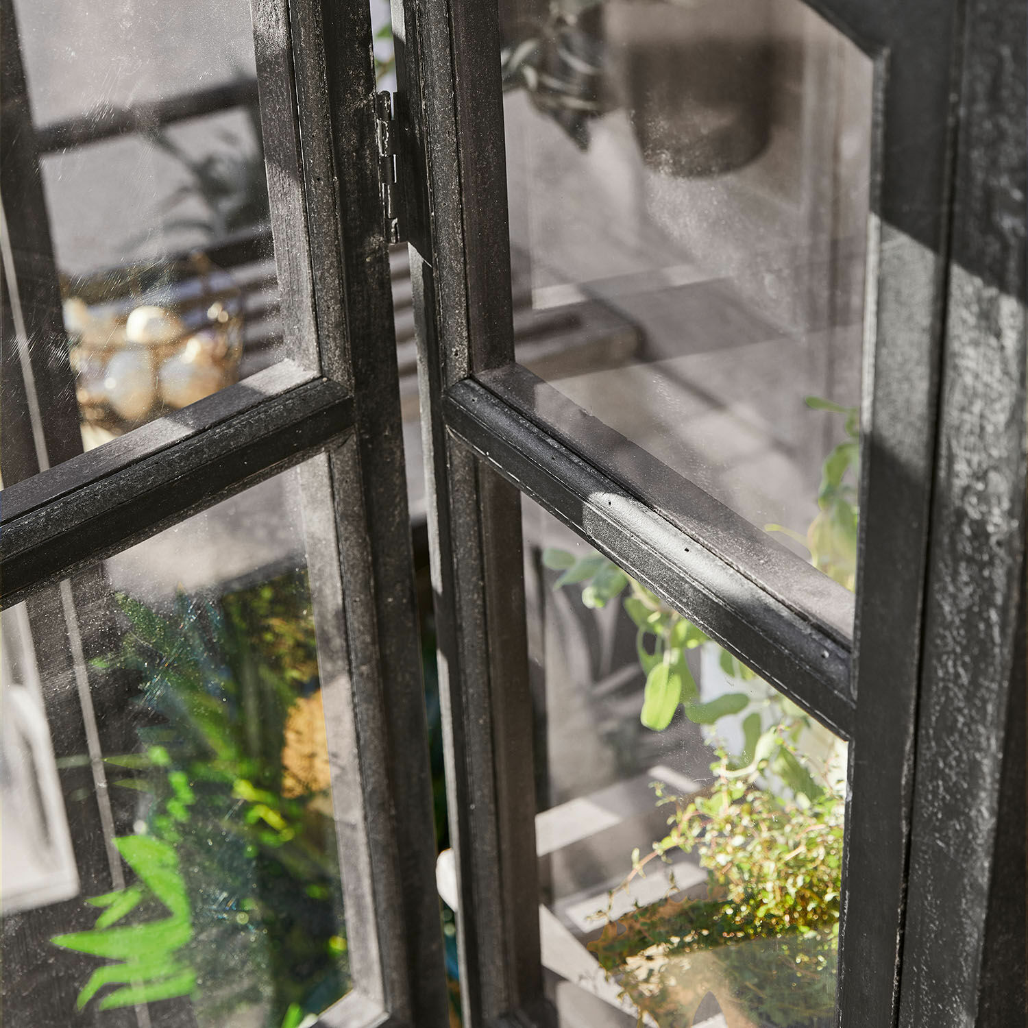 Schwarzer Metallfensterrahmen mit Glasscheiben und grünen Pflanzen im Hintergrund, Industrie-Stil