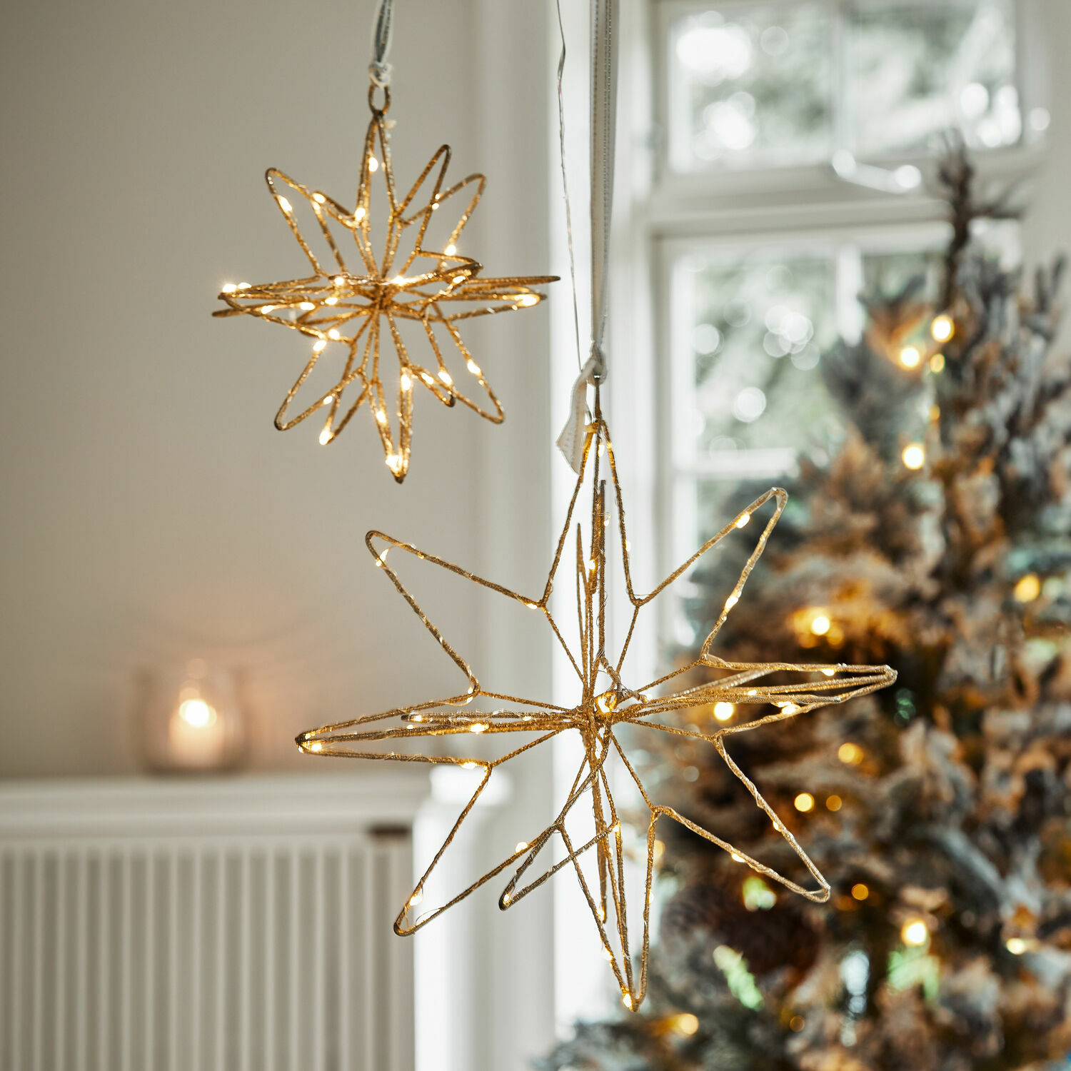 Goldene Stern-Dekorationen mit LED-Beleuchtung vor weihnachtlichem Hintergrund mit Tannenbaum