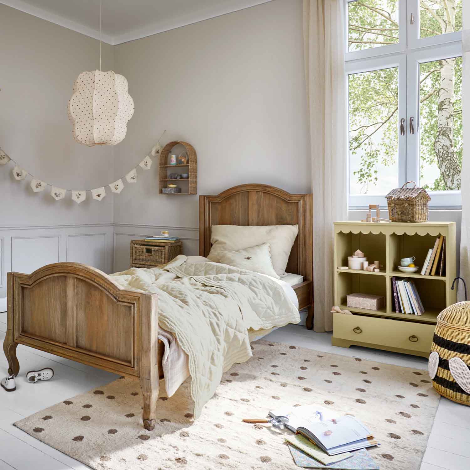 Kinderbett aus Holz in Naturfarbe mit beiger Bettdecke und pastellfarbenem Spielzeugschrank im hellen Zimmer