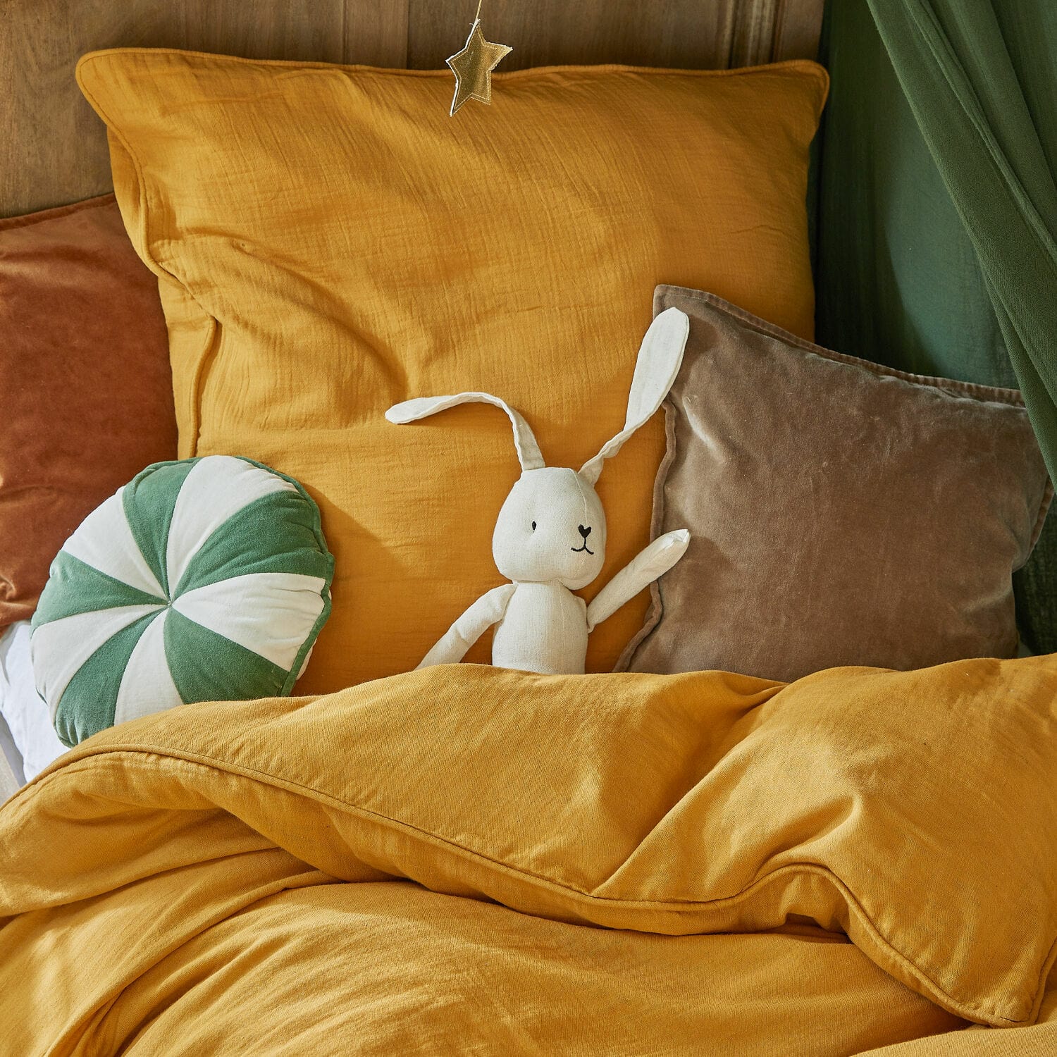 Senfgelbe Bettwäsche und Kissen mit samtigem Kissen und weißem Plüschhasen auf dem Bett