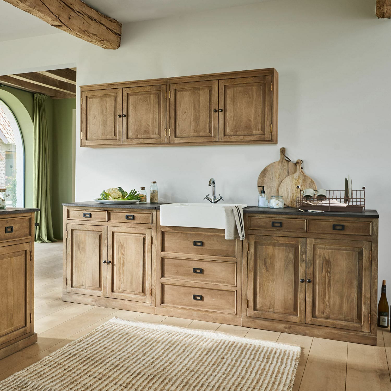 Küche mit Holzschränken und weißem Keramikspülbecken, natürliche Holztöne und schwarze Griffe