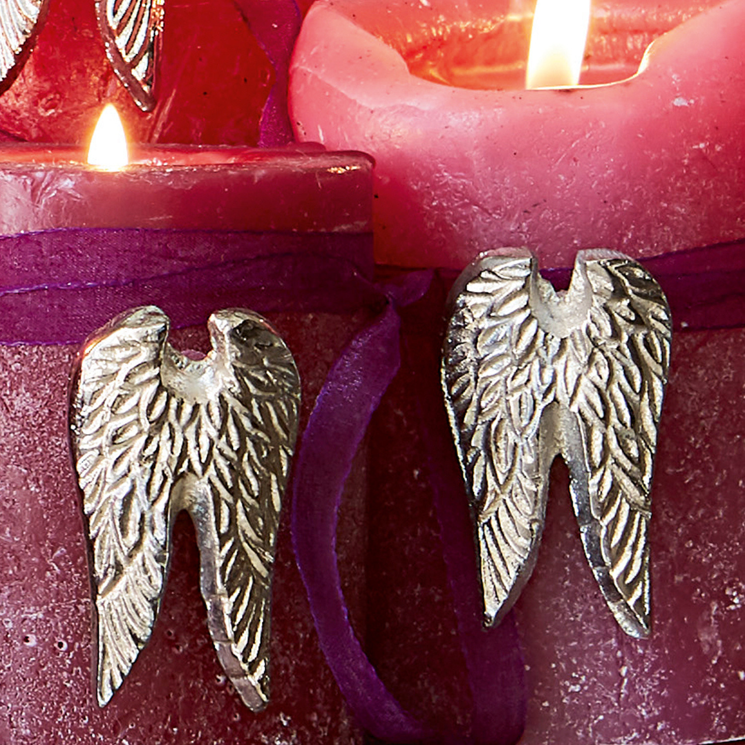 Zwei silberne Metall-Engelsflügel auf bordeauxfarbenen Kerzen mit violettem Band, Wohnaccessoire