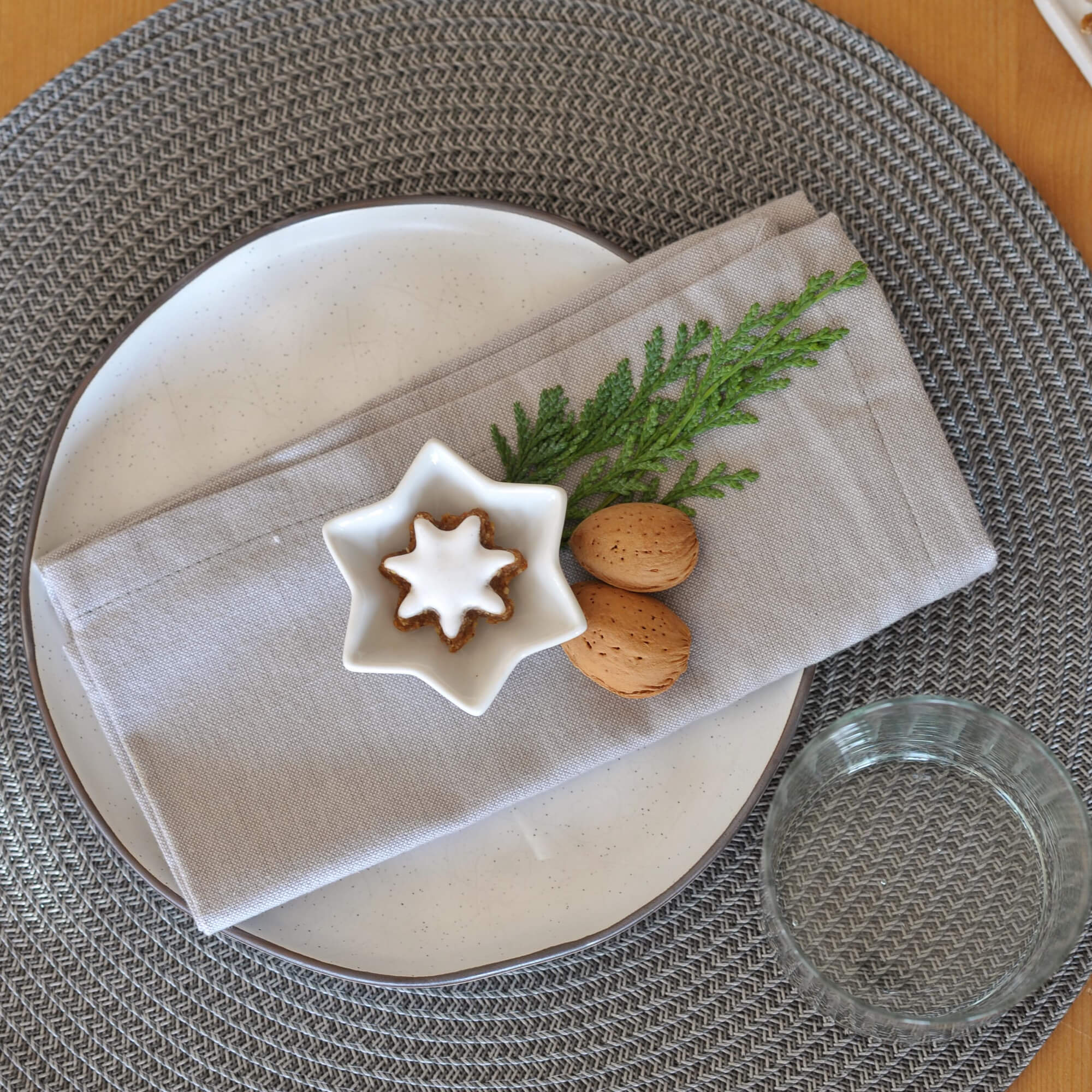 Graue geflochtene Tischunterlage mit weißem Teller, Leinenserviette und Weihnachtsdeko