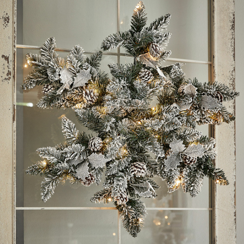 Weihnachtliche Deko aus verschneiten Tannenzweigen mit Zapfen und integrierten LED-Lichtern