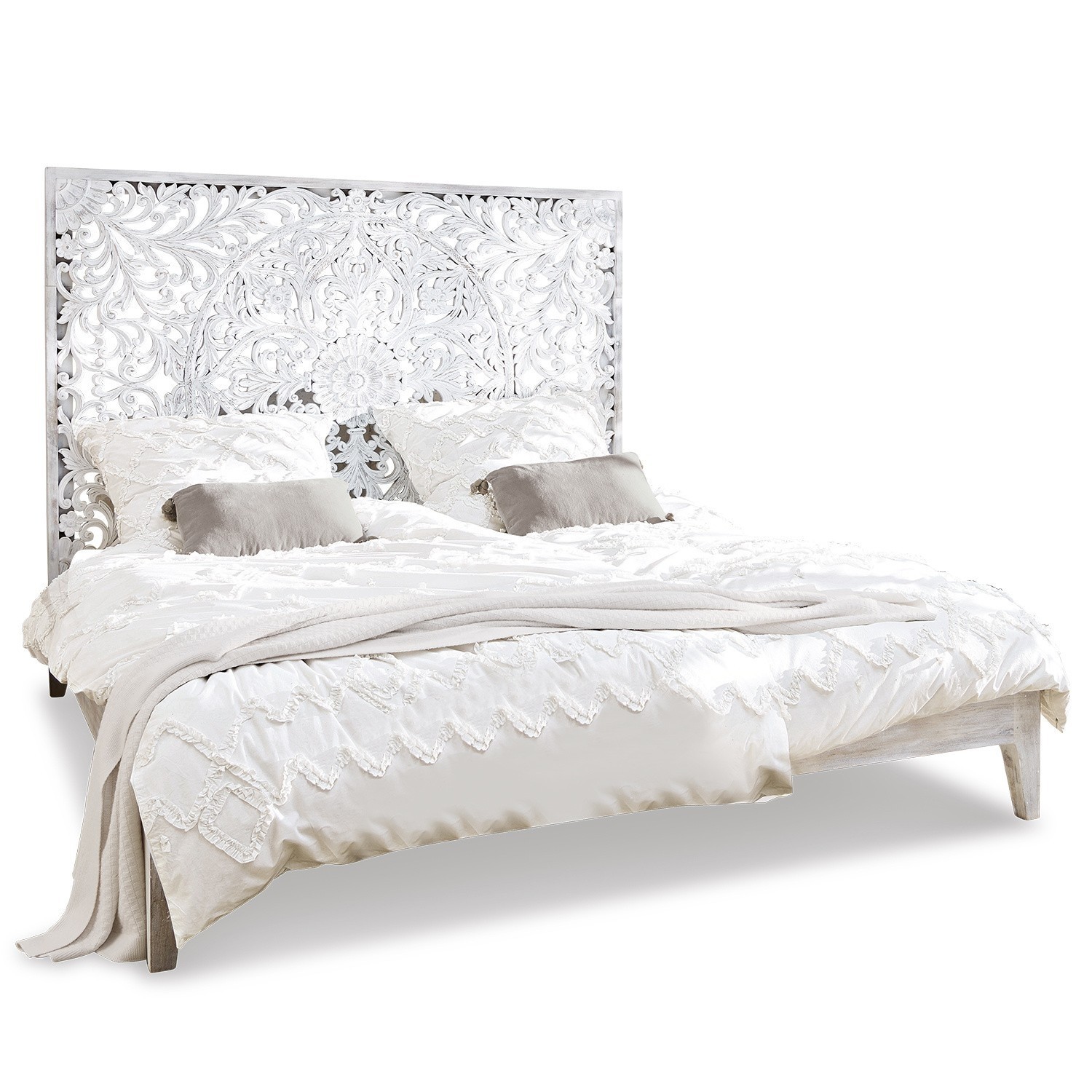 Bett mit weiß geschnitztem Holz-Kopfteil und heller Boho-Bettwäsche aus Baumwolle
