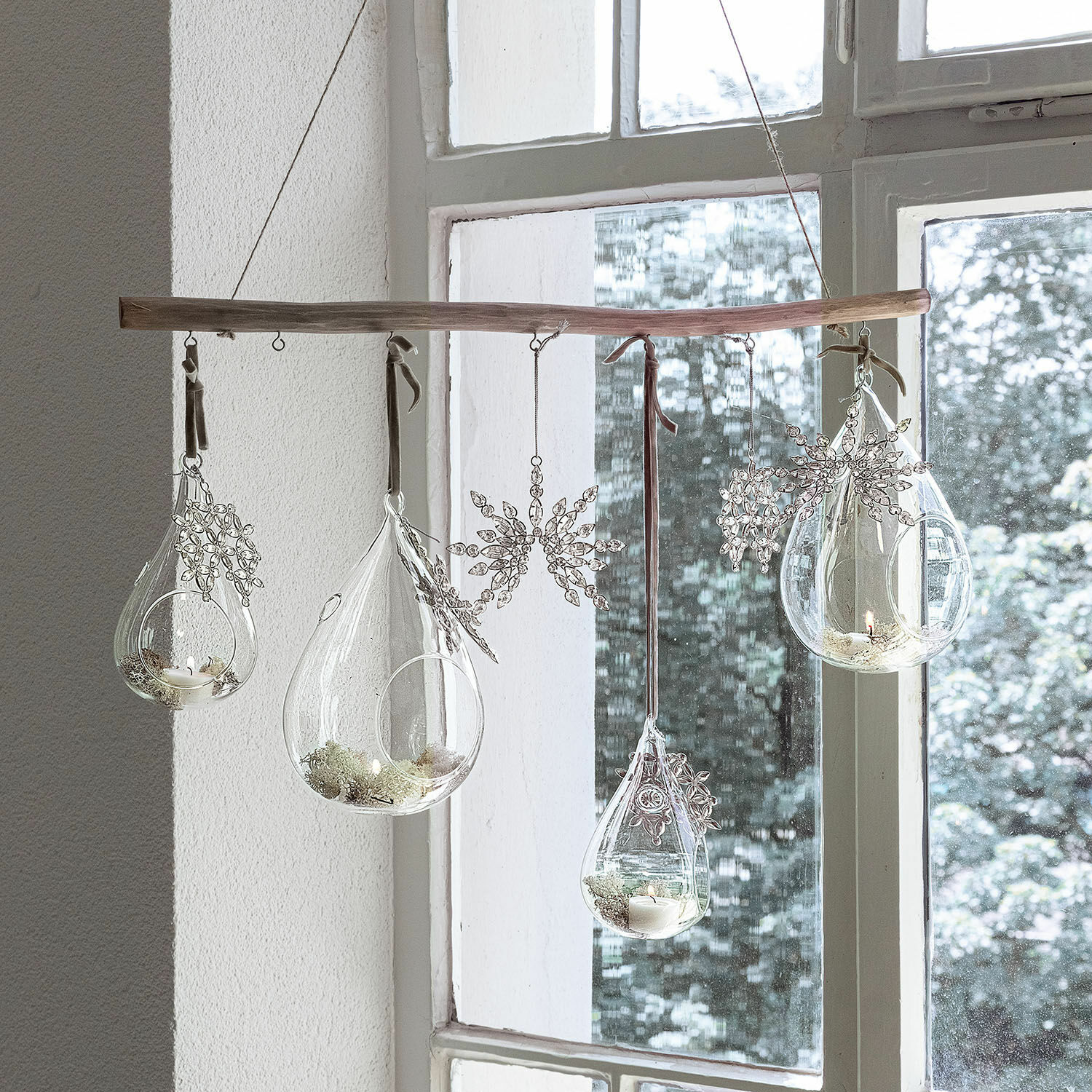 Hängende Glas-Teelichthalter mit Schneeflocken-Dekor an Holzstab vor Fenster