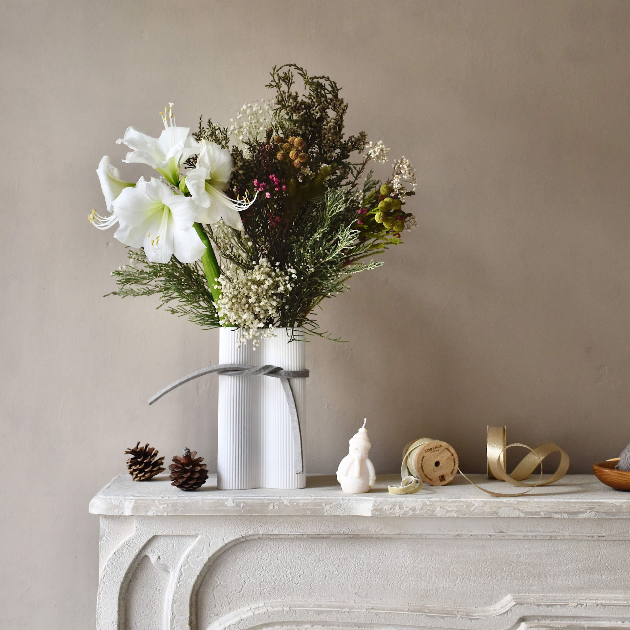Weißer Keramikvase mit weißen Blumen und grünen Zweigen auf einem dekorativen weißen Kamin
