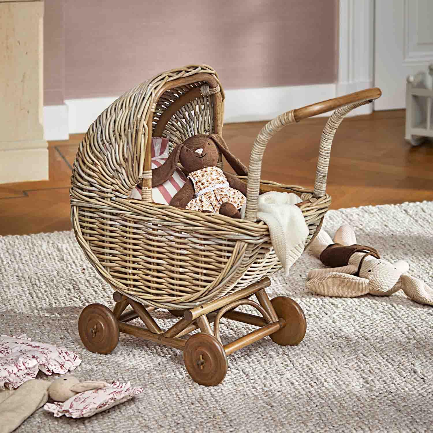 Wickelwagen aus Rattan mit braunem Kuschelhäschen und weißer Decke auf grauem Teppich