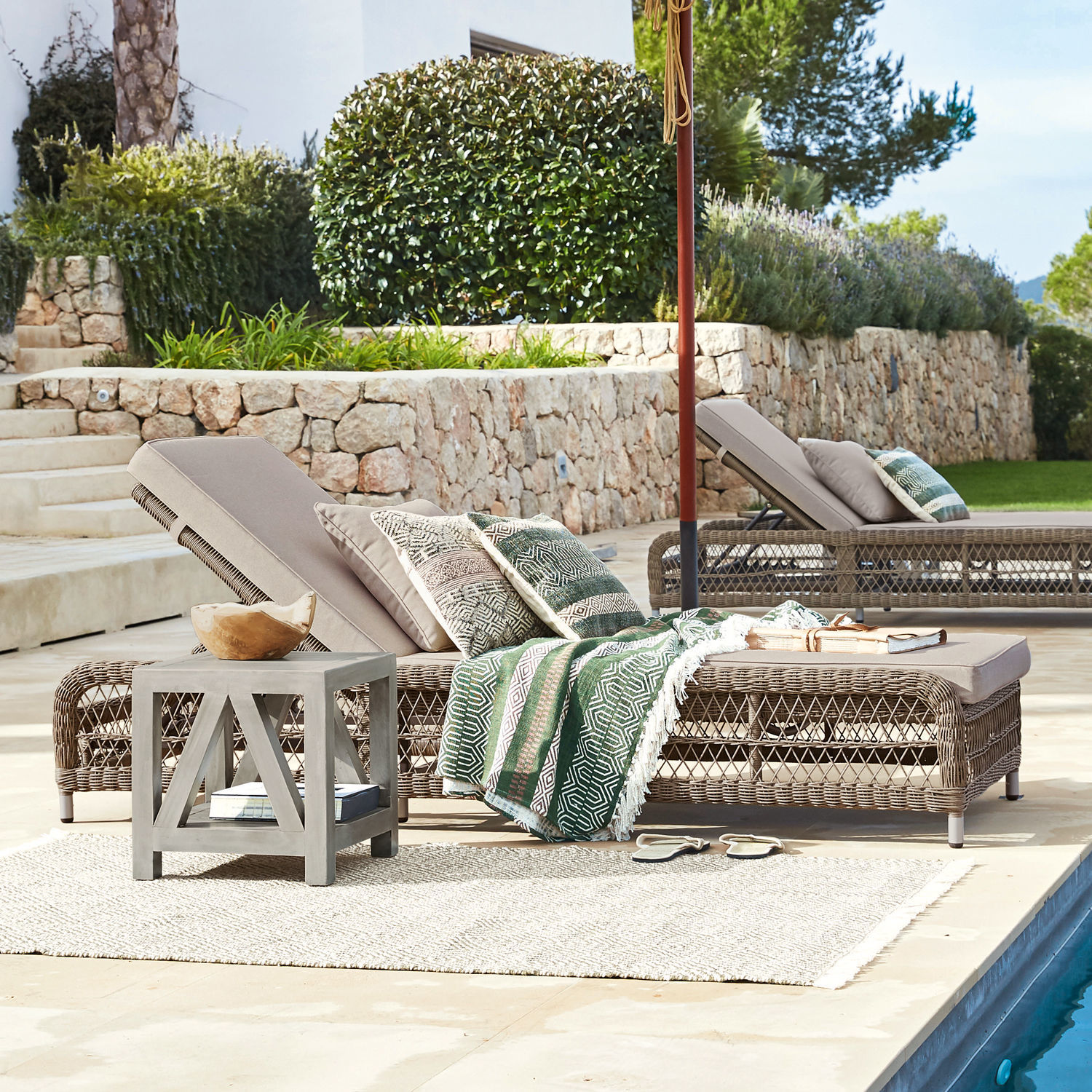 Taupefarbener Rattan-Liegestuhl mit Kissen und grünem Deckenmuster am Pool