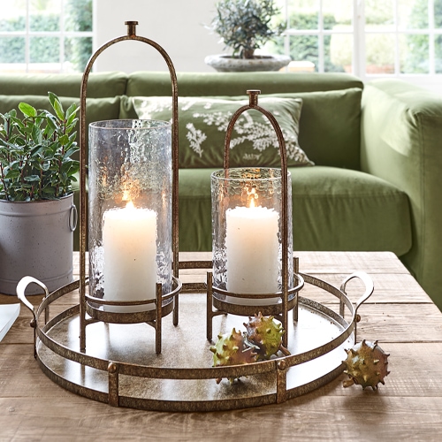 Metalltablett mit zwei Glaslaternen und weißen Kerzen auf hellem Holztisch im Wohnzimmer