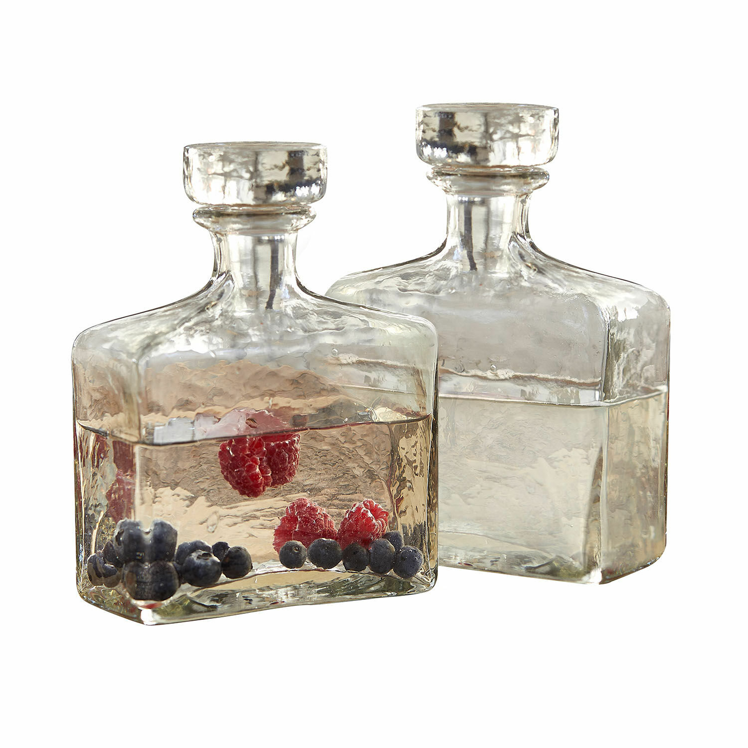 Zwei transparente Glasflaschen mit Stopfen, gefüllt mit Wasser und roten sowie blauen Beeren