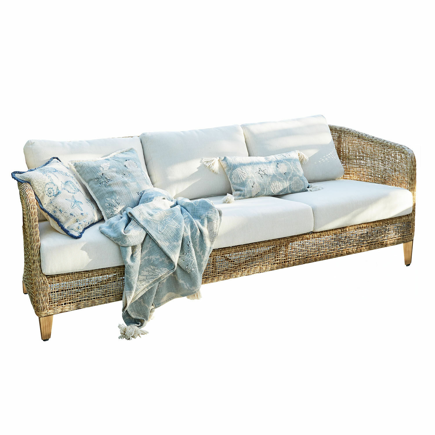 Rattansofa mit cremefarbenen Kissen und blauem Decken mit Meeresmotiven für Wohnzimmer
