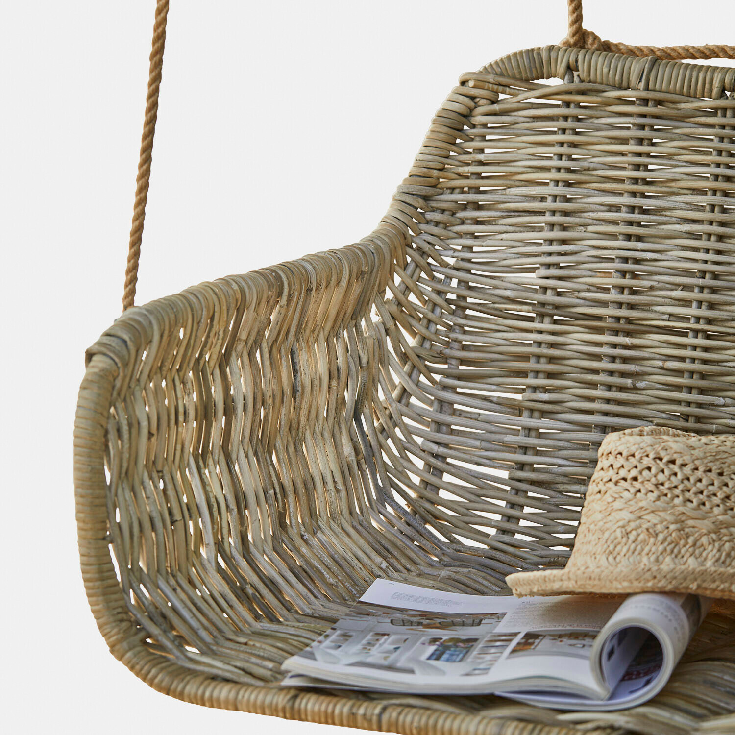 Natürliche Rattan-Hängeschaukel mit Magazin und Strohhut auf dem Sitz
