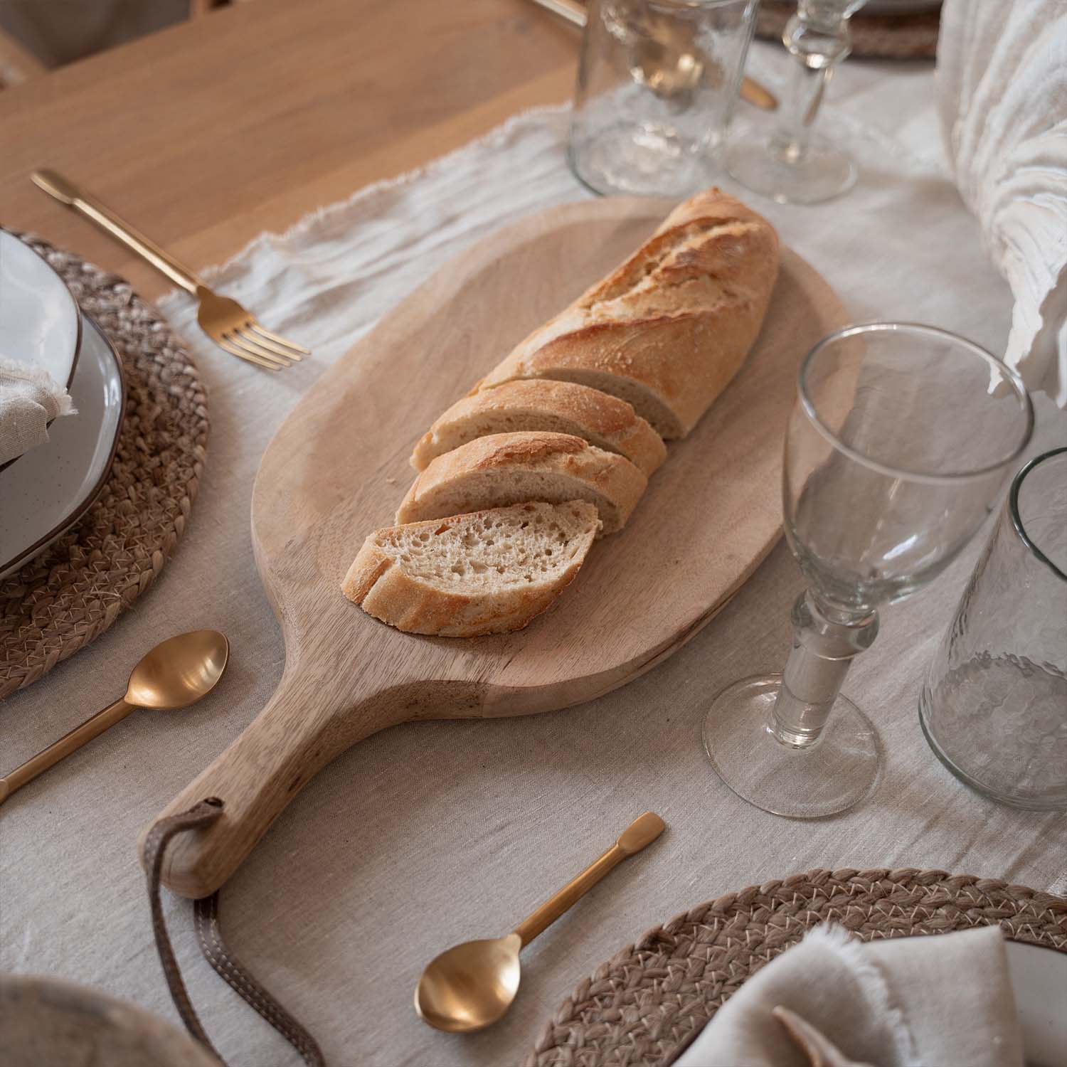 Holzbrett mit aufgeschnittener Baguette auf Tisch mit natürlichem Leinentuch und goldenen Bestecken