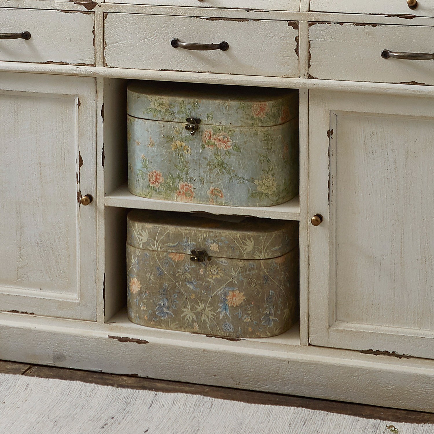 Zwei dekorative Metallboxen mit Blumenmuster in Pastellfarben auf weißem Holzregal