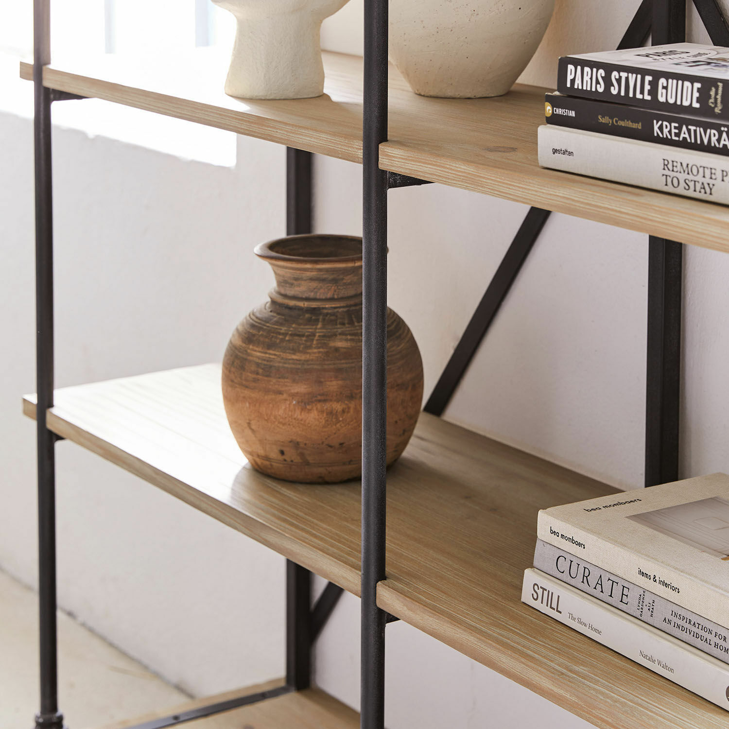 Regal aus hellem Holz mit schwarzem Metallrahmen, Keramikvase und dekorativen Büchern