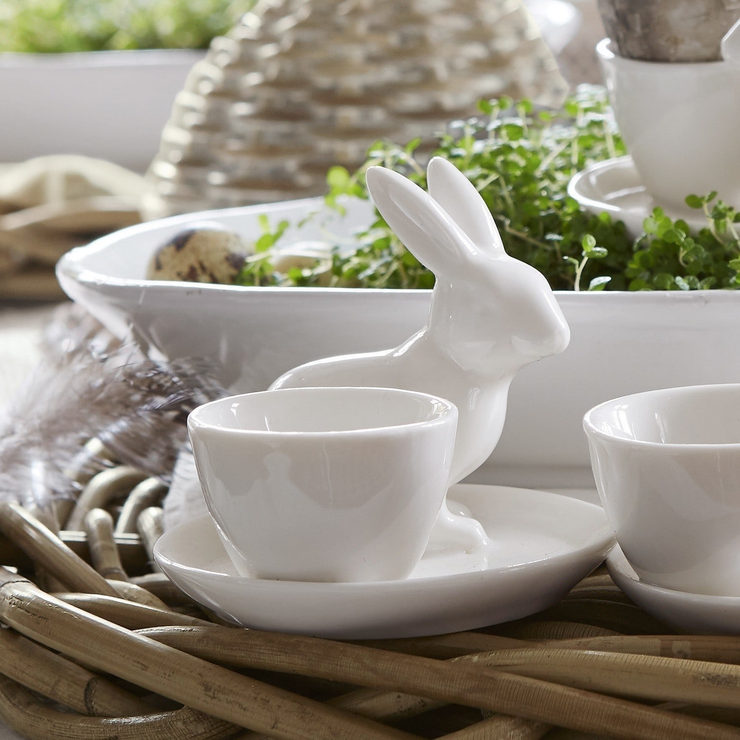 Weiße Keramiktasse mit Untertasse und Hasendekor auf geflochtenem Hintergrund, Tischdekoration