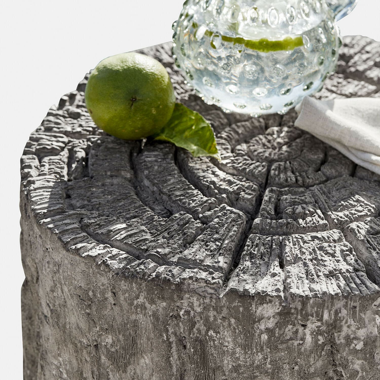 Beistelltisch aus grauem Beton mit Baumstammstruktur, Limette und Wasserglas darauf