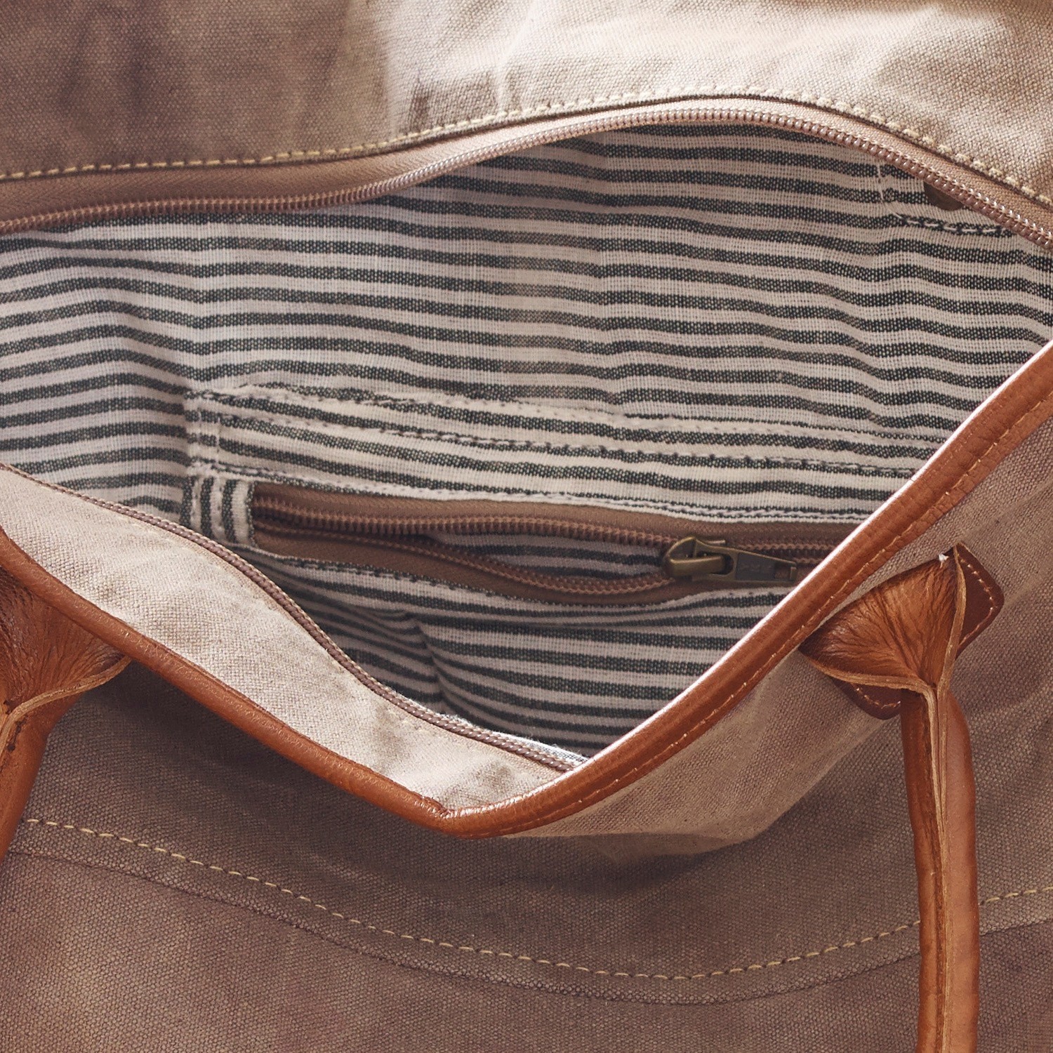 Beige Stofftasche mit braunen Ledergriffen, gestreiftes Innenfutter und Reißverschlusstasche innen