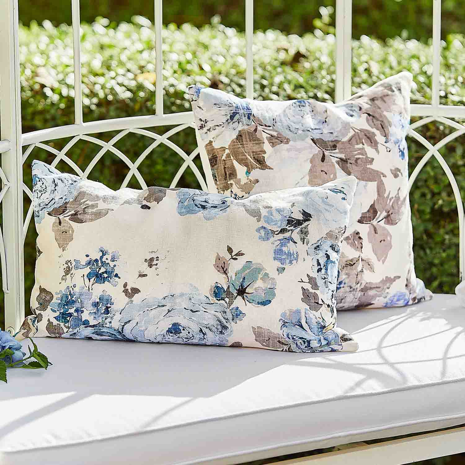 Zwei dekorative Baumwollkissen mit blau-beigem Blumenmuster auf weißer Gartenbank