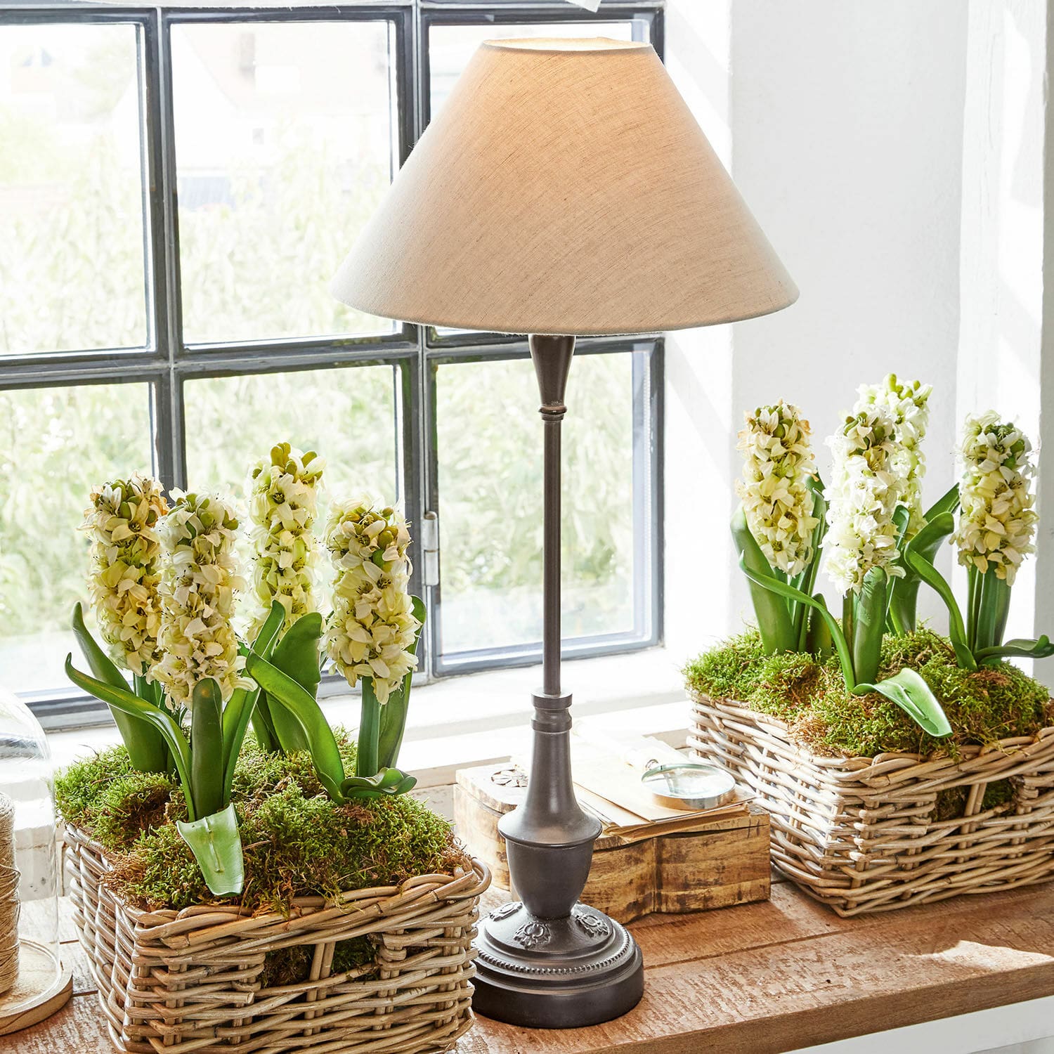 Tischlampe Barnwell Tischlampe mit Metallfuß und beigem Lampenschirm neben Weidenkörben mit weißen Blumen und Moos