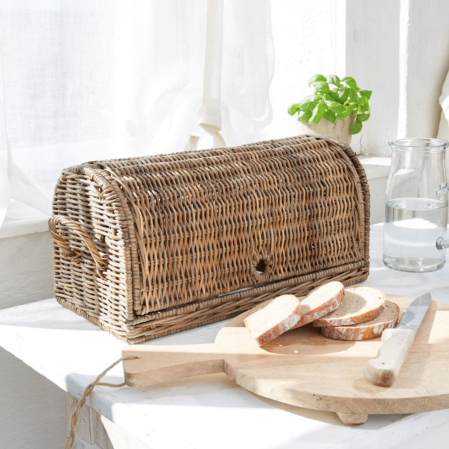 Brotkasten aus natürlichem Rattan auf Küchentisch mit geschnittenem Brot und Messer