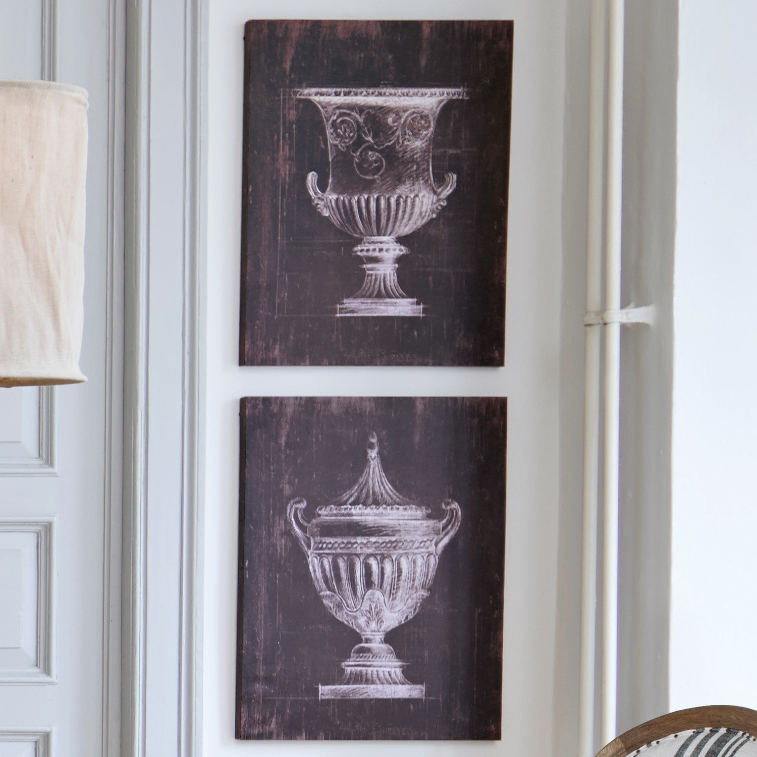 Zwei schwarze Bilder mit weißen Zeichnungen antiker Vasen an heller Wand im Raum