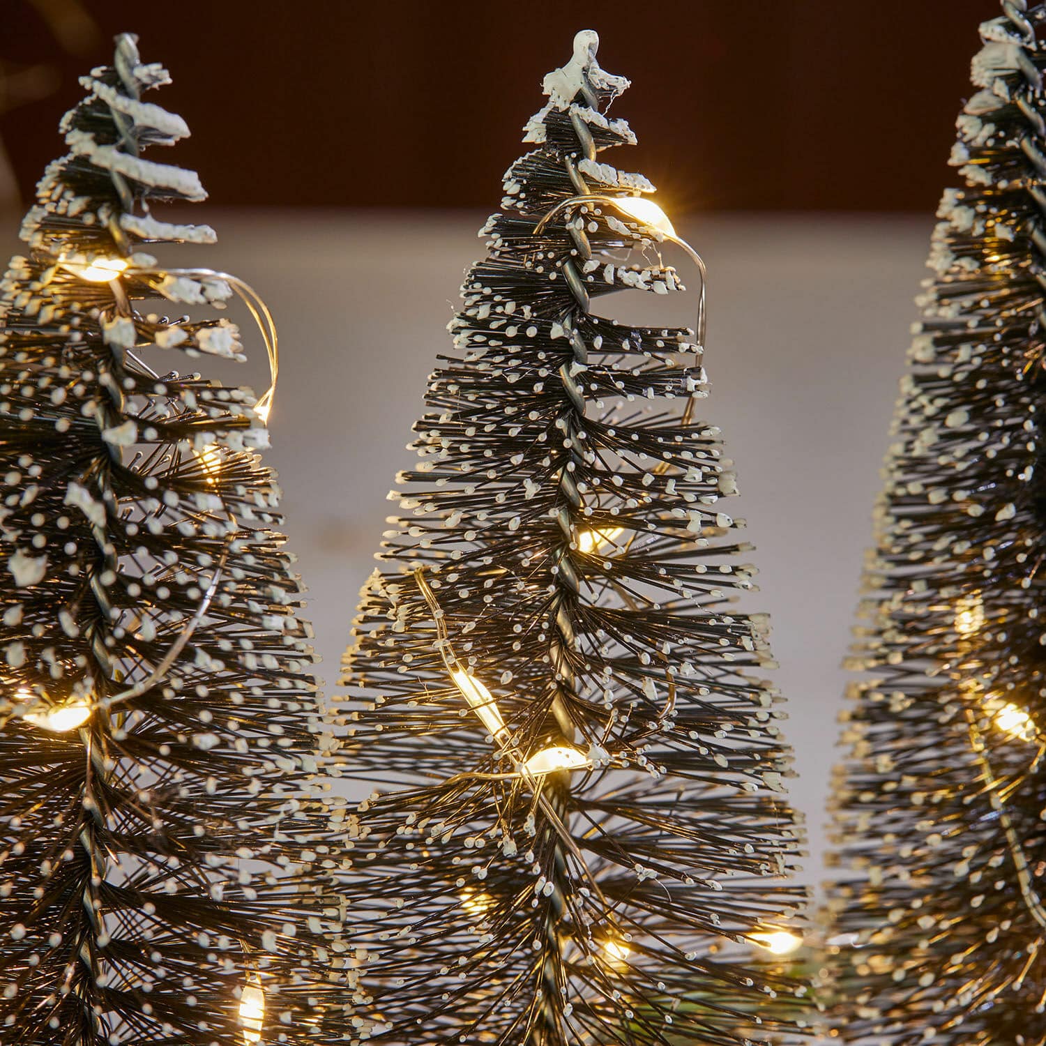 Dekorative Weihnachtsbäume aus Metall mit weißen Spitzen und warmen LED-Lichtern als Deko