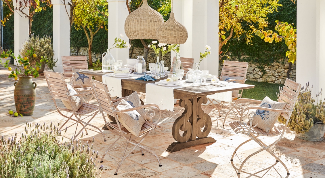 Gartenmöbel-Set mit Holztisch und Metallstühlen auf Terrasse mit Dekorationen und Kissen