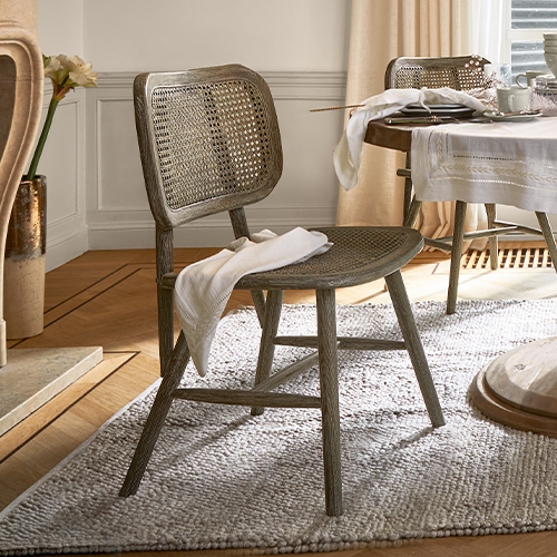 Stuhl aus Holz und Rattan in Naturfarbe auf Teppich in hellem Wohnzimmer mit gedecktem Tisch