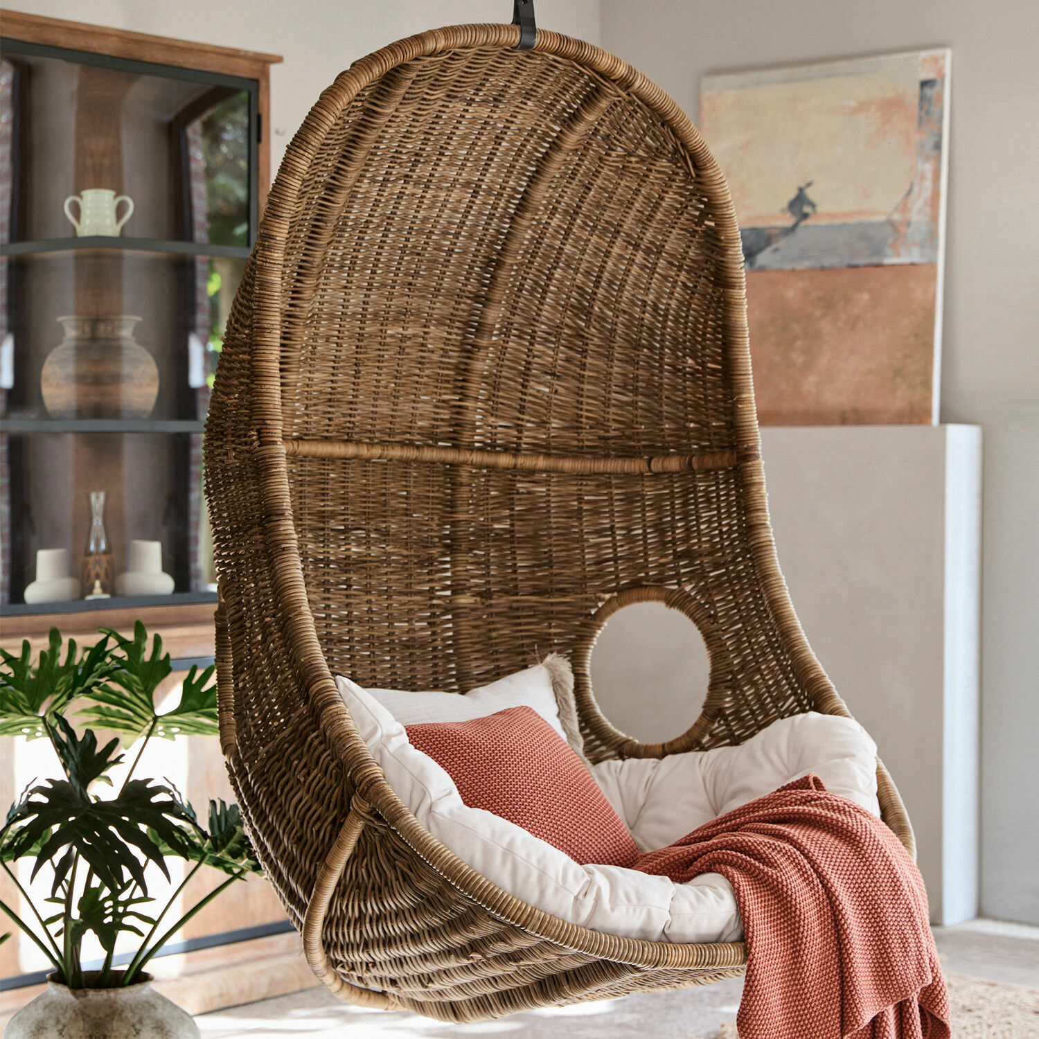 Hängesessel aus natürlichem Rattan mit weißem Kissen und roter Decke für gemütliches Wohnen