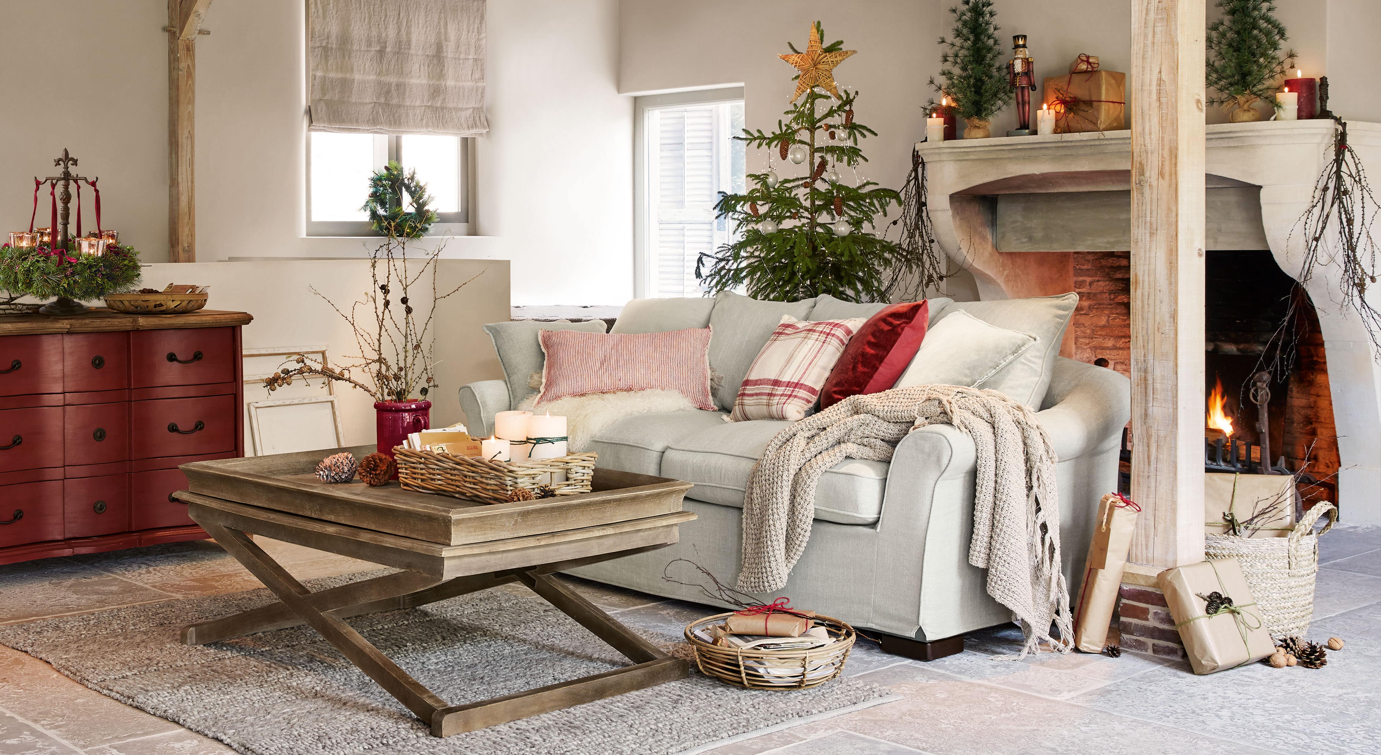 Gemütliches Wohnzimmer mit hellgrauem Sofa, Holztisch und Weihnachtsdekoration mit Tannenbaum und Kaminfeuer