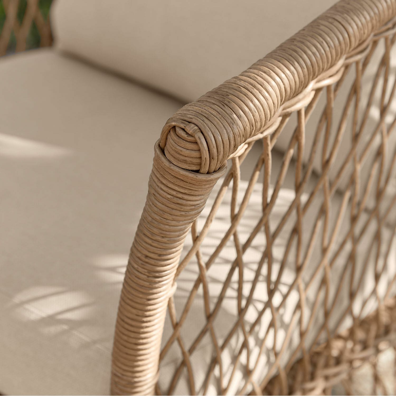 Detail eines naturfarbenen Rattan-Fauteuils mit hellem Stoffpolster für Wohn- und Außenbereich