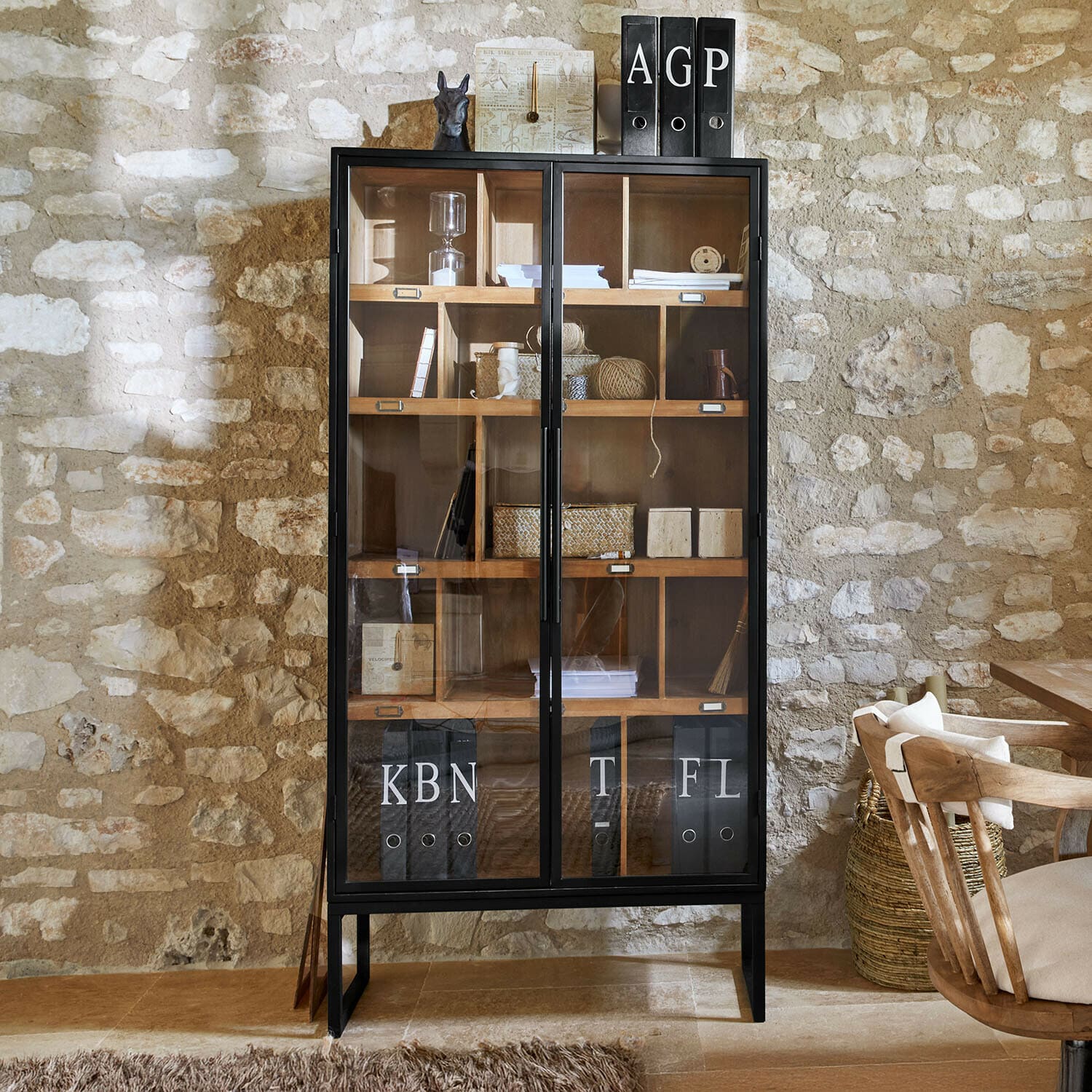 Schwarzer Metall-Vitrinenschrank mit Holzregalen und Glastüren in rustikalem Raum mit Steinwand
