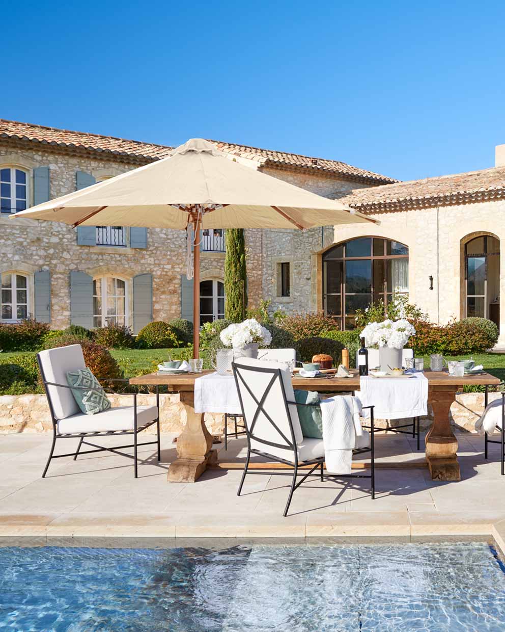 Gartenmöbel-Set mit Holztisch und beigem Sonnenschirm am Pool im rustikalen Stil
