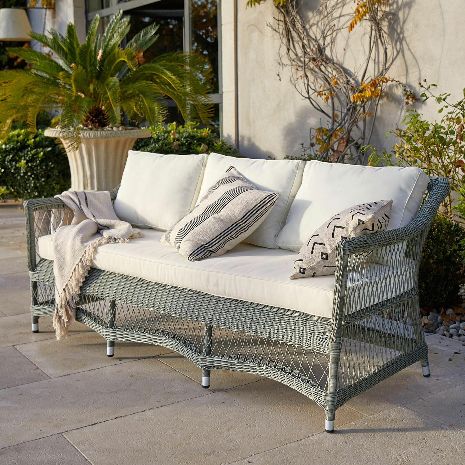 Gartensofa aus grauem Geflecht mit cremefarbenen Polstern und gemusterten Dekokissen