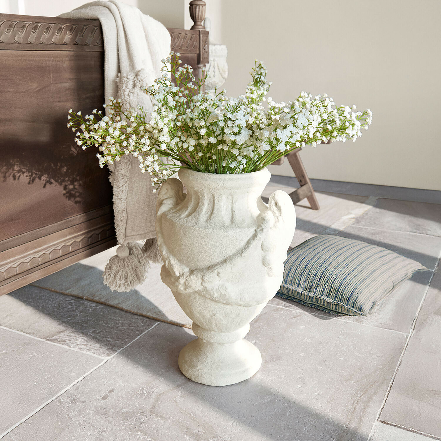 Weiße Keramikvase mit dekorativem Muster und weißen Blumen auf Steinboden