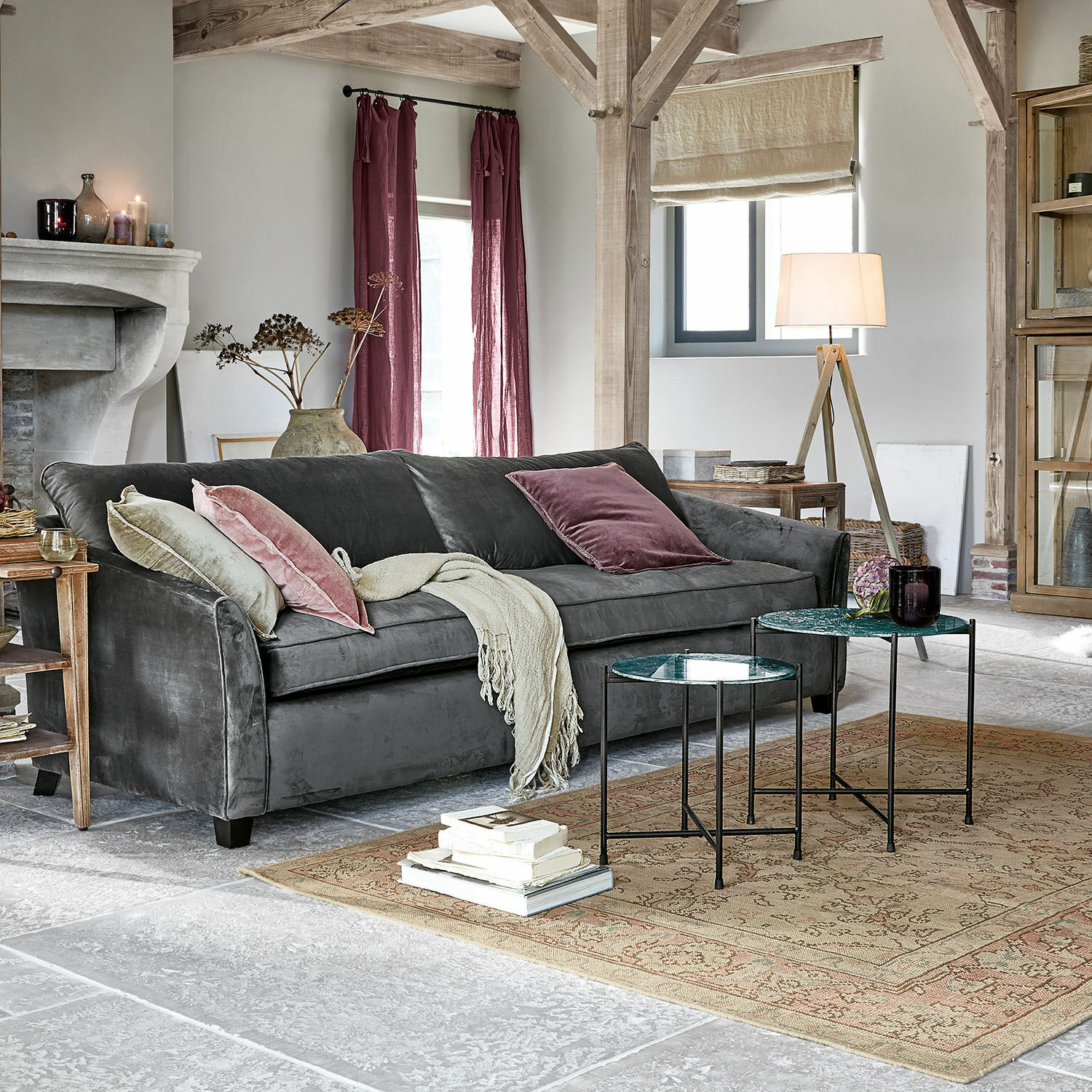 Graues Samtsofa mit rosa Kissen und beiger Decke in stilvollem Wohnzimmer mit Holzbalken