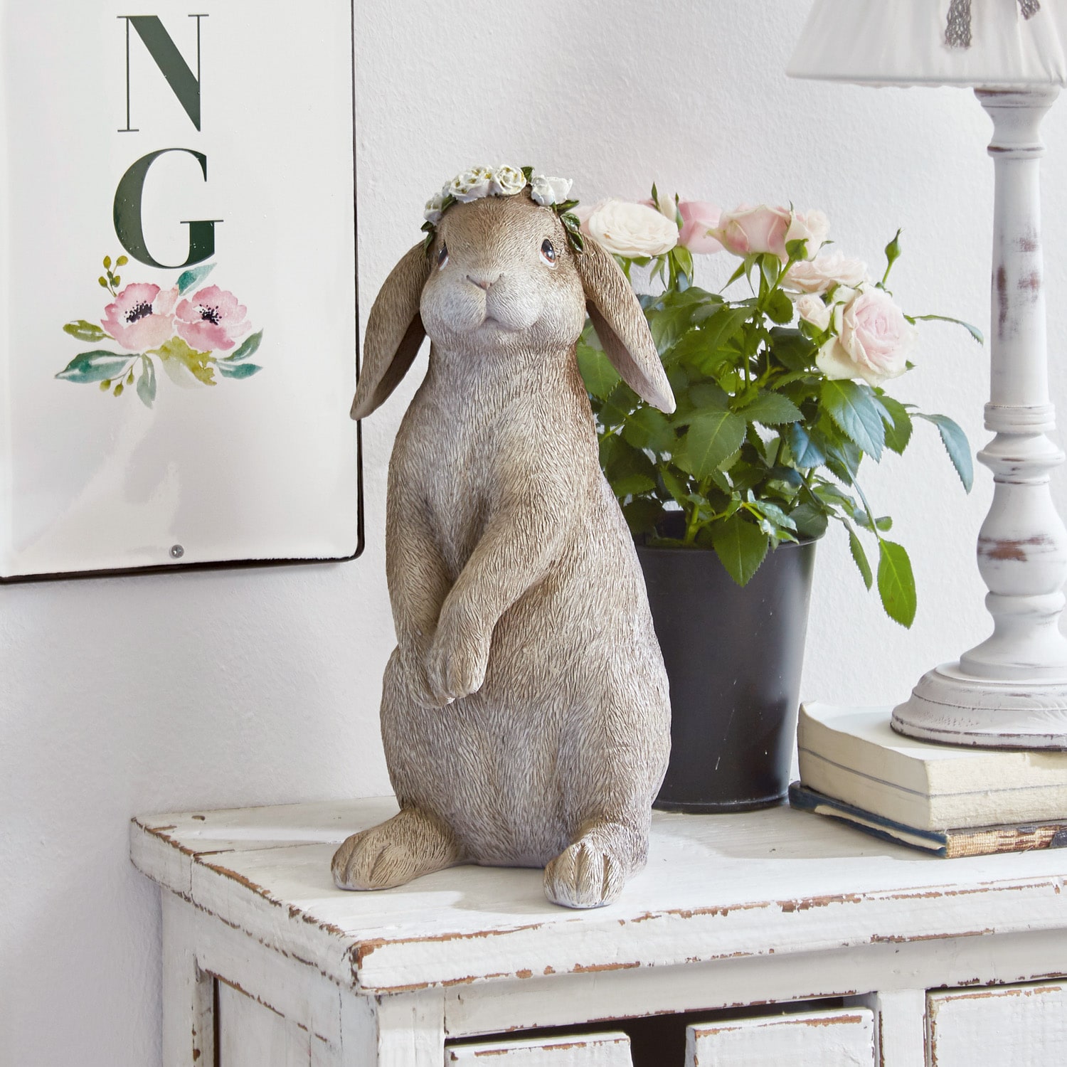 Dekorative Hasenfigur in Beige mit Blumenkranz auf weißem Holzkommode stehend