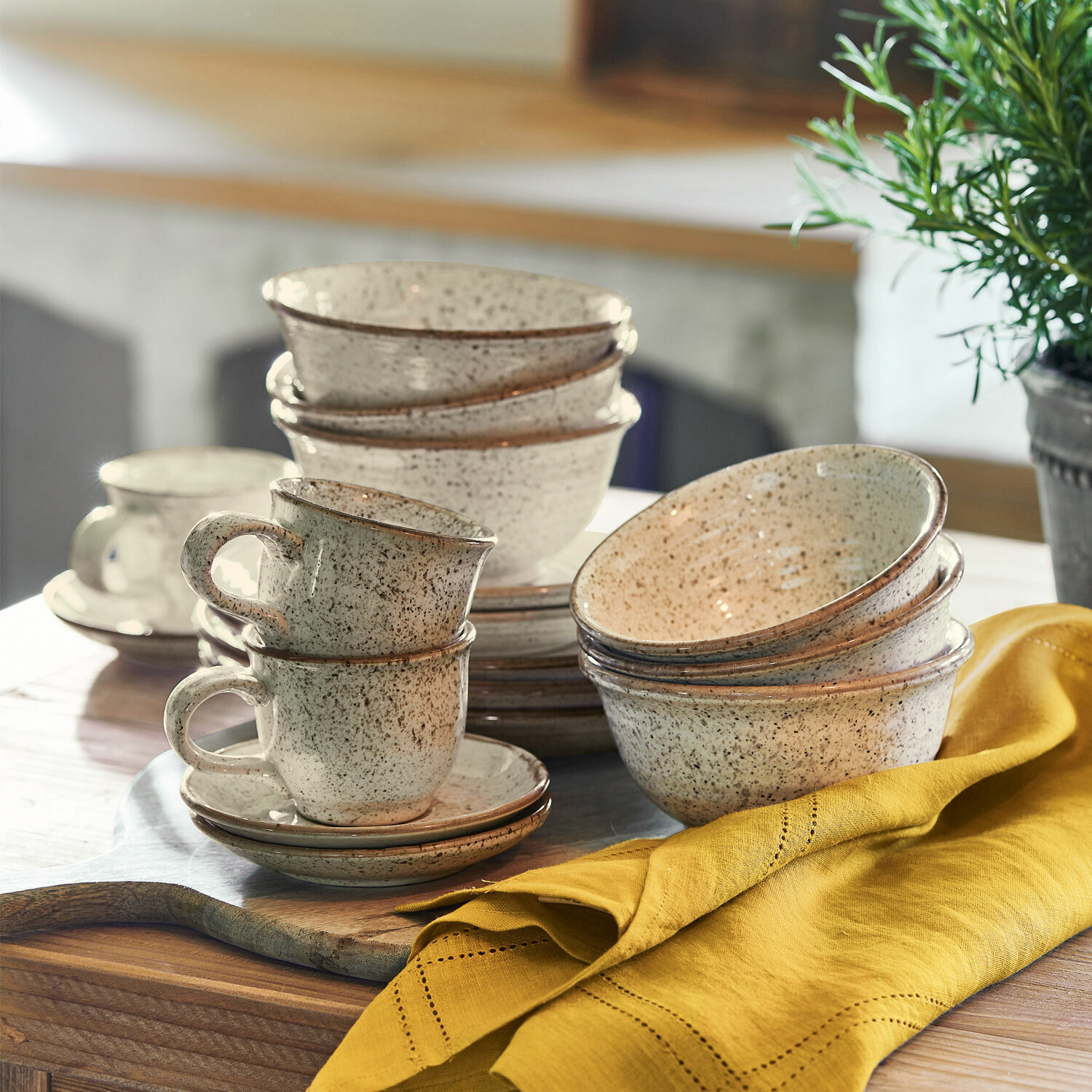Set aus cremefarbenen Keramikschalen und Tassen mit braunen Sprenkeln auf rustikalem Holztisch