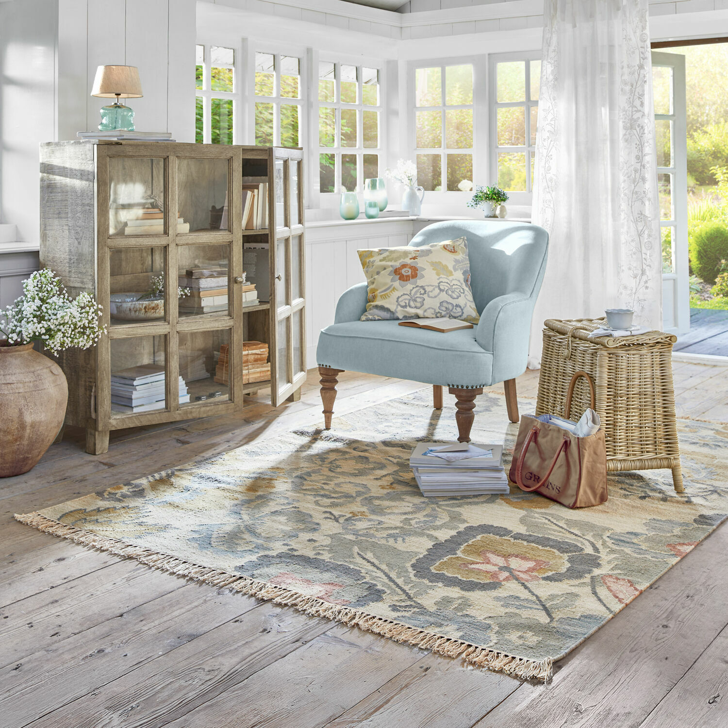 Teppich Sussex Helles Wohnzimmer mit hellblauem Sessel, Holzvitrine und floralem Teppich auf hellem Holzboden