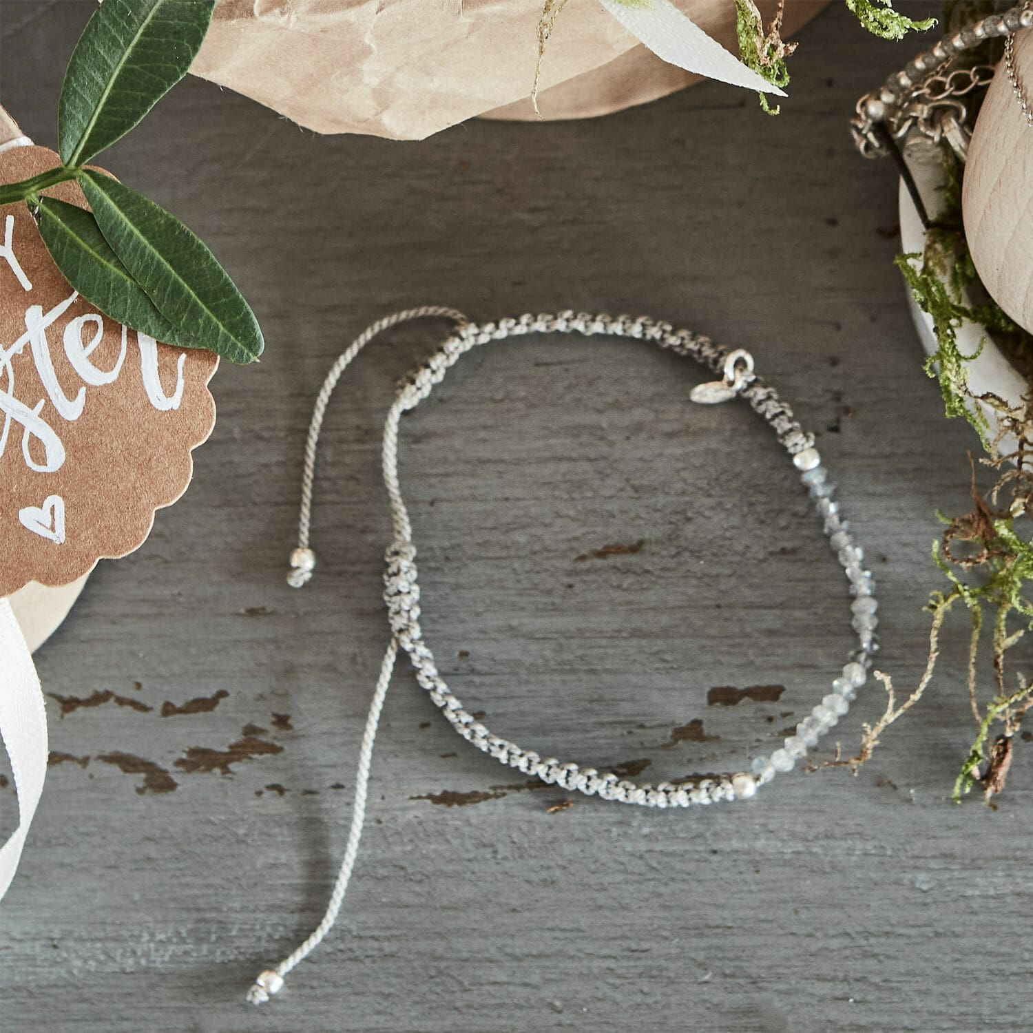 Feines Armband aus grauem Band und Steinen auf grauem Untergrund, modischer Damenschmuck