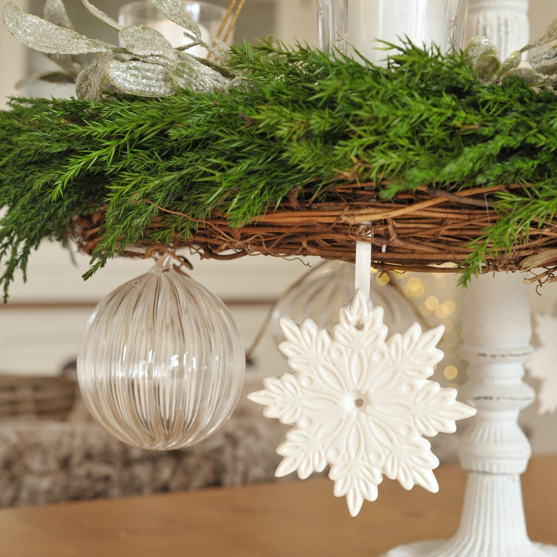 Weißer Keramik-Schneeflockenanhänger und transparente Glaskugel an grünem Adventskranz aus Weide