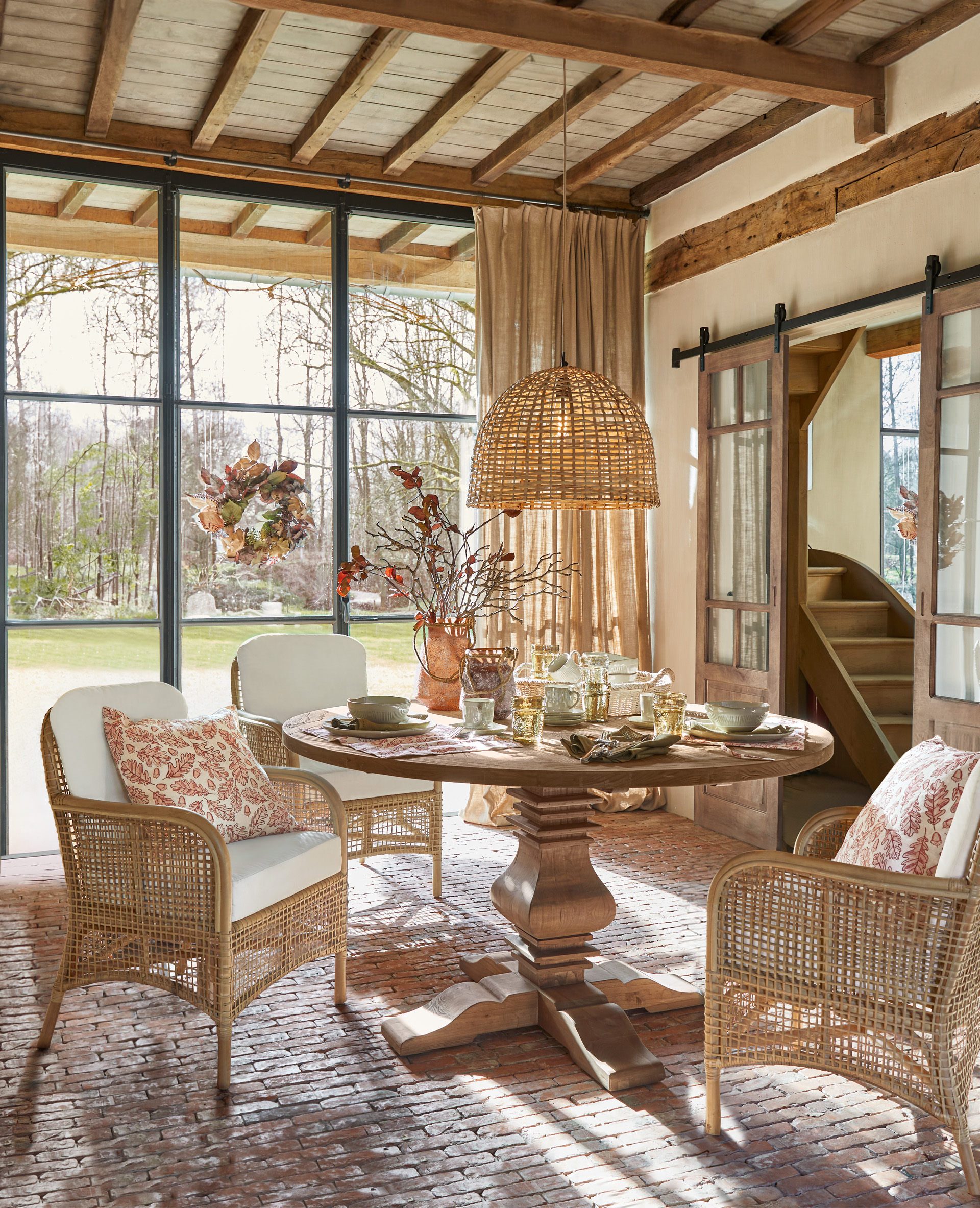 Esszimmer mit rundem Holztisch und Rattanstühlen mit weißen Kissen und Dekorationen