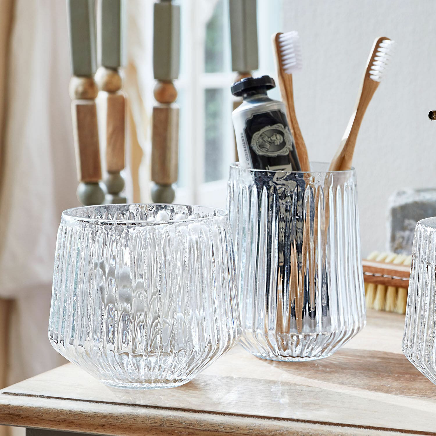 Transparente Glasbehälter mit geriffeltem Muster auf Badezimmerablage mit Bambuszahnbürsten