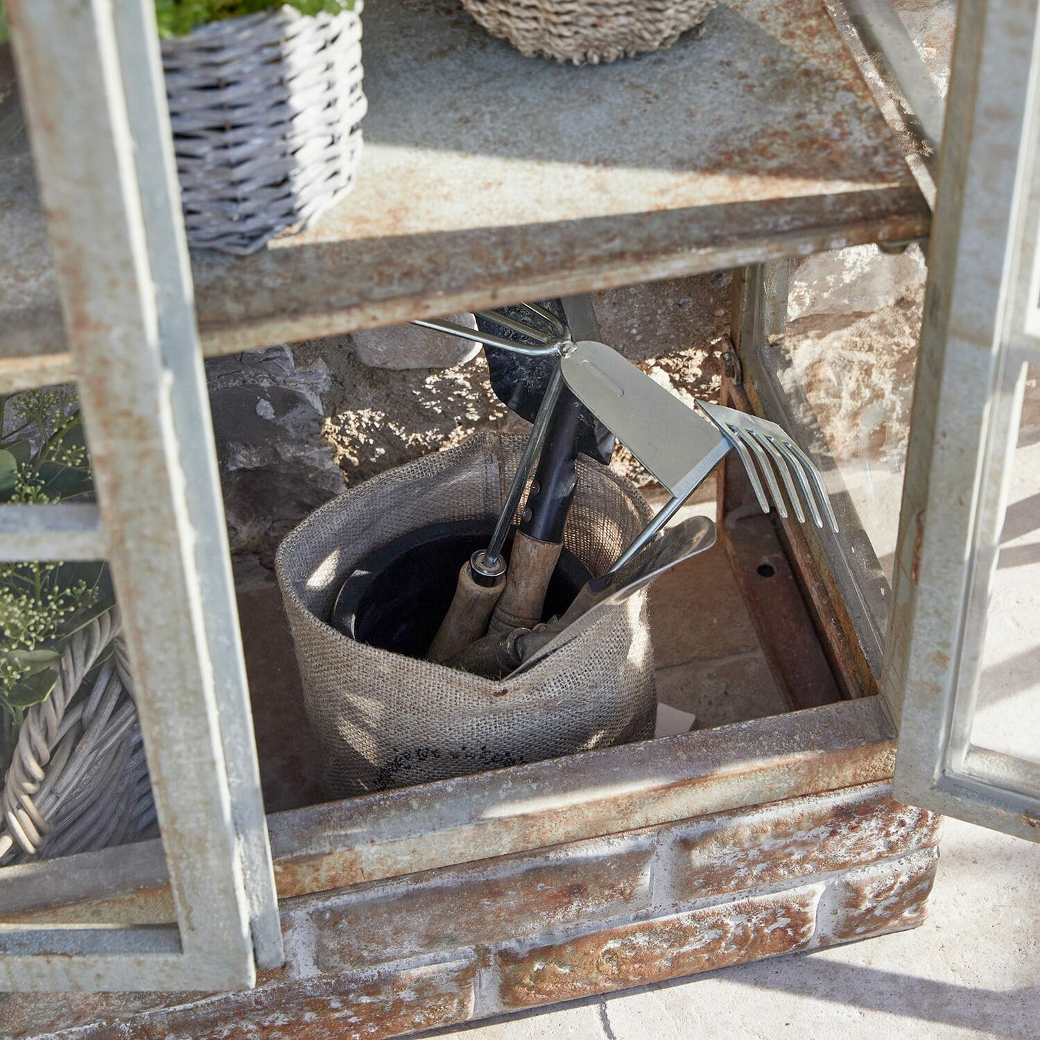 Gartengeräte mit Holzgriffen in einem Leinensack in einer rostigen Metallvitrine auf Steinboden
