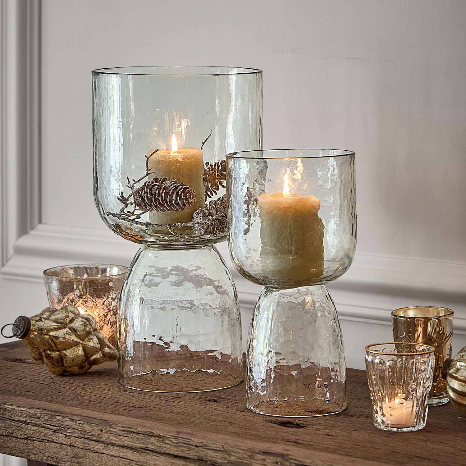 Glaswindlichter mit Struktur, beigen Kerzen und dekorativen Kiefernzapfen auf Holztisch