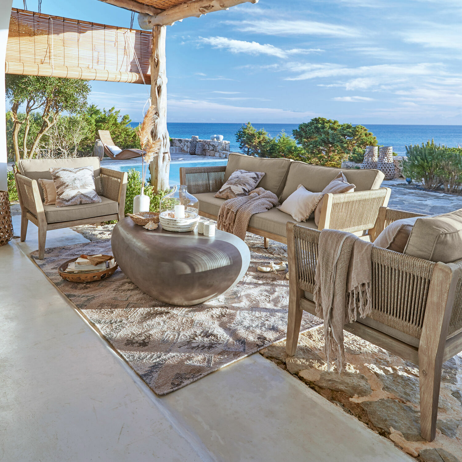 Outdoor-Möbelset mit beigen Polstern und grauem Steintisch auf Terrasse mit Meerblick